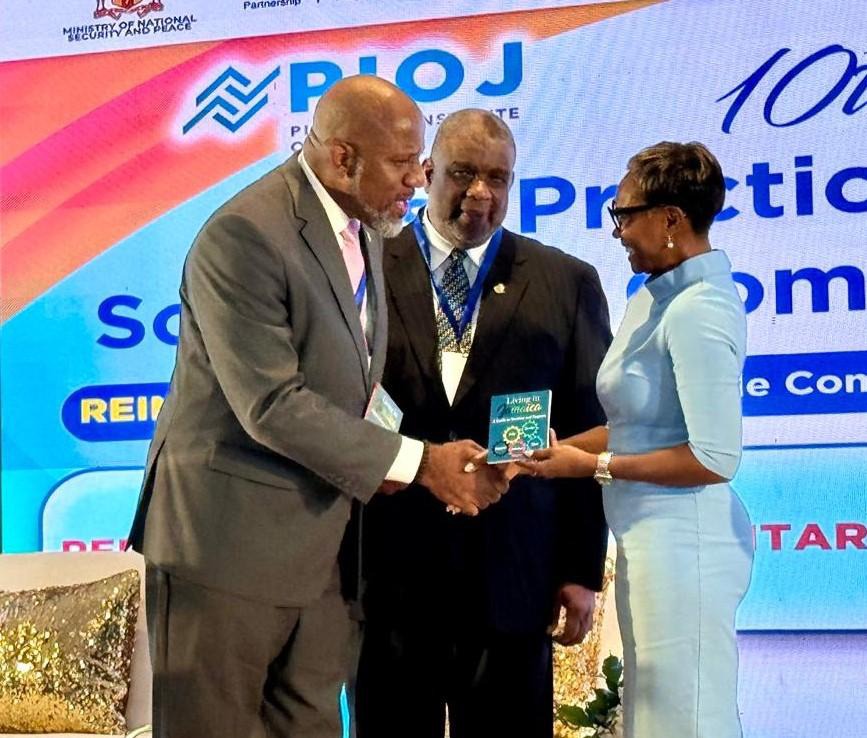 Minister of State in the Ministry of National Security and Peace, the Hon. Juliet Cuthbert-Flynn (right), accepts a handbook entitled ‘Living in Jamaica, A Guide to Service and Support’ from the Director General, Planning Institute of Jamaica, Dr. Wayne Henry (left), while Permanent Secretary in the Ministry of Health and Wellness, Mr. Errol Greene (centre) looks on. Minister Cuthbert-Flynn gave remarks at the opening session of the two-day 10th National Symposium on Best Practices for Social and Community 