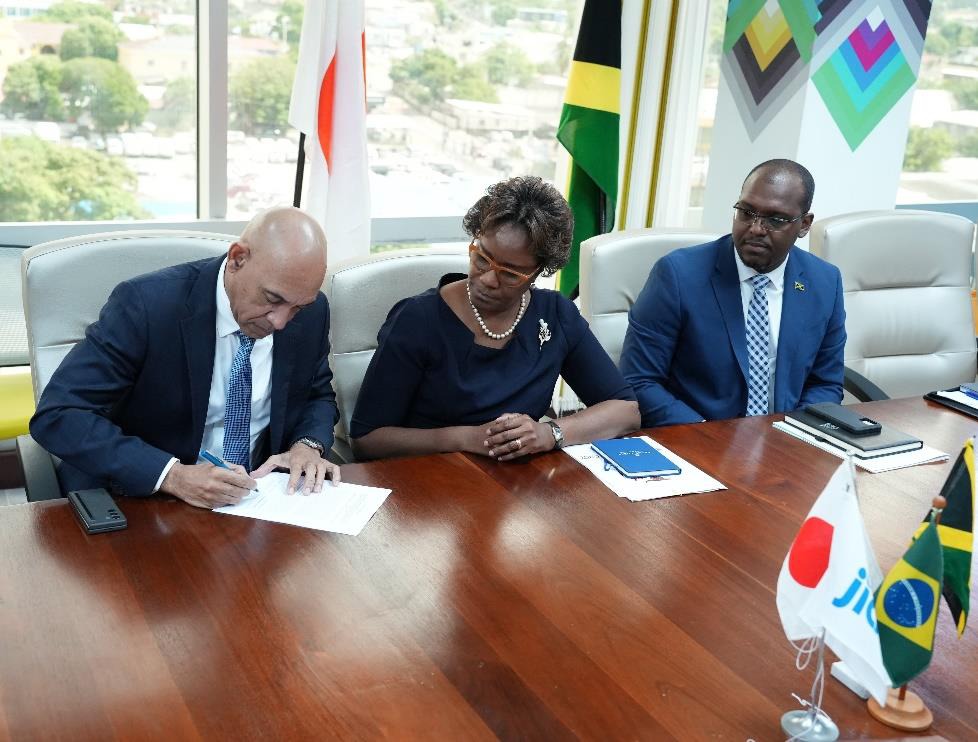 Permanent Secretary in the Ministry of National Security, Ambassador Alison Stone Roofe looks on as Commissioner of Police, Major General Antony Anderson signs a trilateral agreement between the Governments of Jamaica, the Federative Republic of Brazil and Japan for community policing training. The signing ceremony was held at the Ministry of National Security in Kingston today (March 1). Chief Technical Director at the Ministry of National Security Michael Morgan also shares in the moment.
