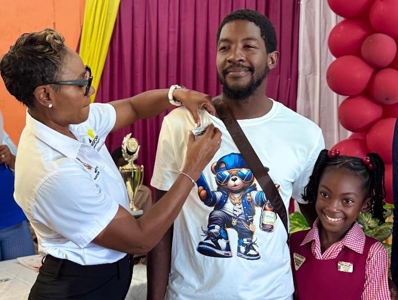 Minister of State in the Ministry of National Security and Peace, the Hon. Juliet Cuthbert-Flynn (left), pins Mr. Brandon Lee, father of honour student Zarahmay Lee (right), for being an outstanding parent at the York Town Primary and Infant School’s Annual Prize Giving Ceremony. Mr Lee was among several parents on hand to celebrate their children’s academic achievements for the last school term.