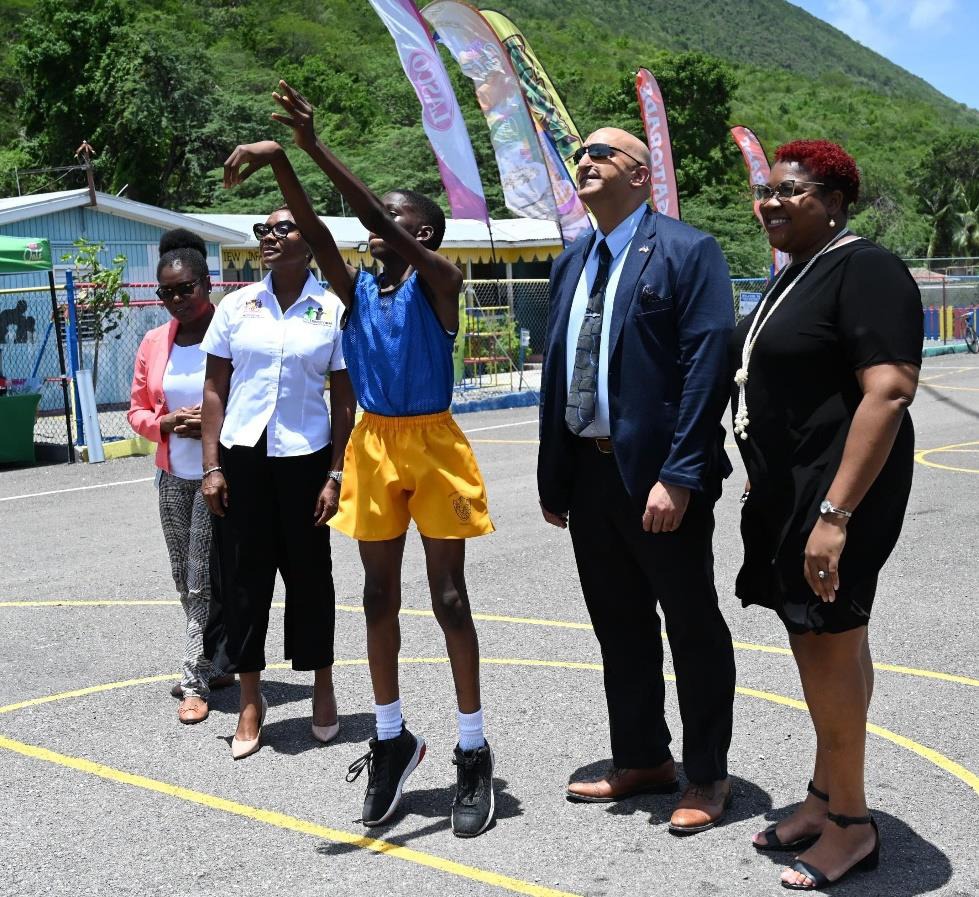Minister of State in the Ministry of National Security, the Hon. Juliet Cuthbert-Flynn, United States Agency for International Development (USAID) Country Representative, Dr. Jaidev Singh, Chief Technical Director in the Ministry of National Security, Shauna Trowers and Principal of the Mountain View Primary School, Michelle Robinson looks on as student of Mavisville Preparatory, Jace Jean takes a shot at the opening of a one day basketball showcase today (June 24). The event was held at the Mountain View P