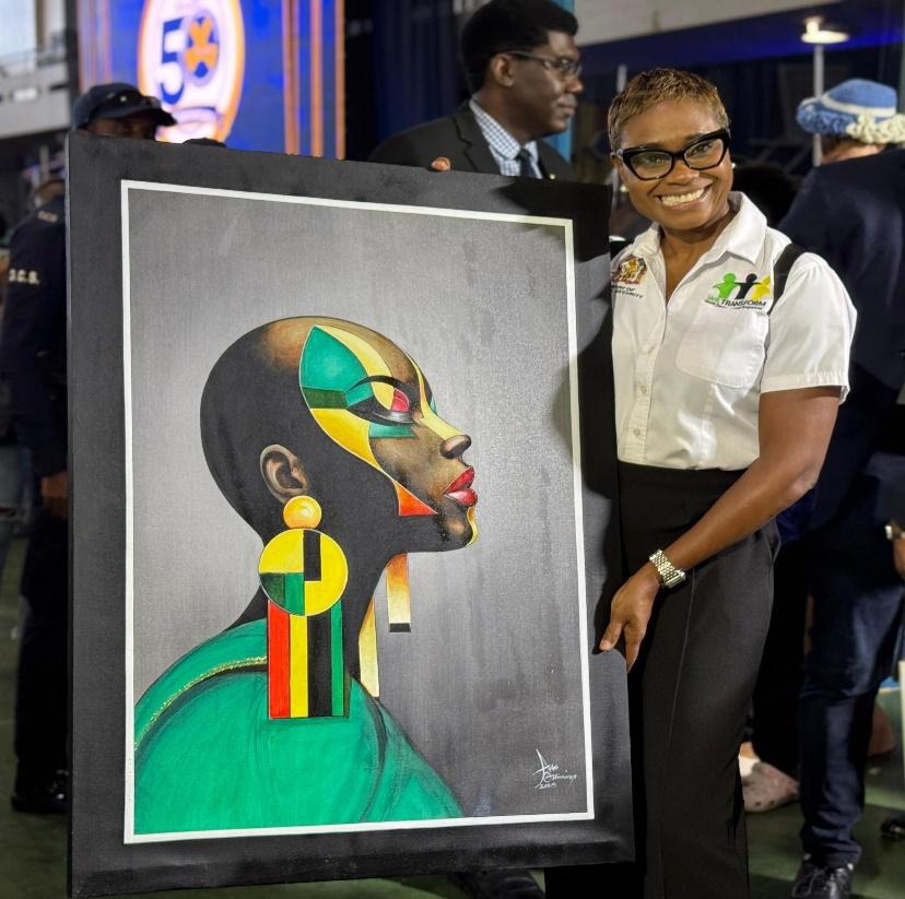 Minister of State in the Ministry of National Security and Peace, the Hon. Juliet Cuthbert Flynn, shows off a painting by an inmate during the DCS 50th Anniversary Opening Ceremony, held on Friday, October 17, at the National Arena in Kingston.